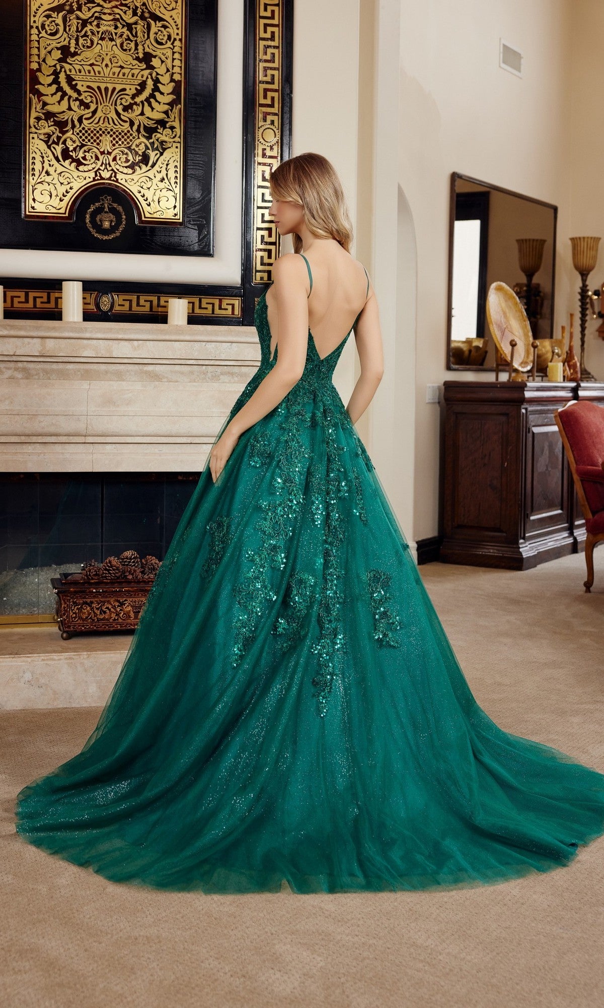 A woman wearing the Nox Anabel H1880 long prom dress with an elegant green a-line skirt and floral embroidery stands facing away in a classic living room.